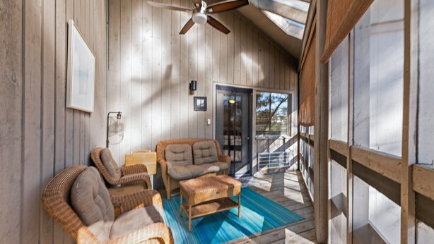 A wooden deck with wicker furniture, a ceiling fan, and a view of the outside.