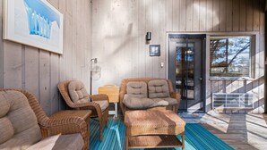 A wooden interior with wicker furniture, a framed picture, and a door leading outside.