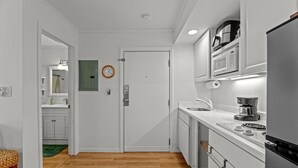 A modern kitchen with white cabinetry, a stainless steel refrigerator, a microwave, and a coffee maker.