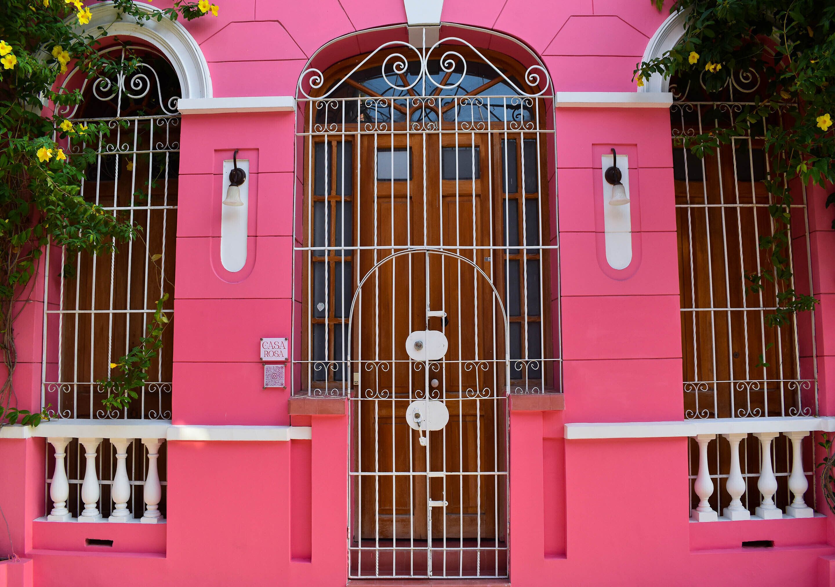 A pink building with a central arched window, flanked by two smaller windows with metal bars.