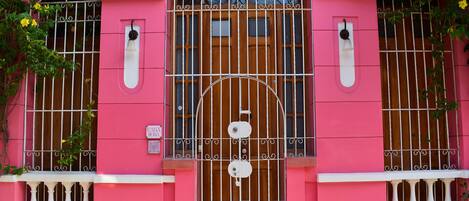 A pink building with a central arched window, flanked by two smaller windows with metal bars.