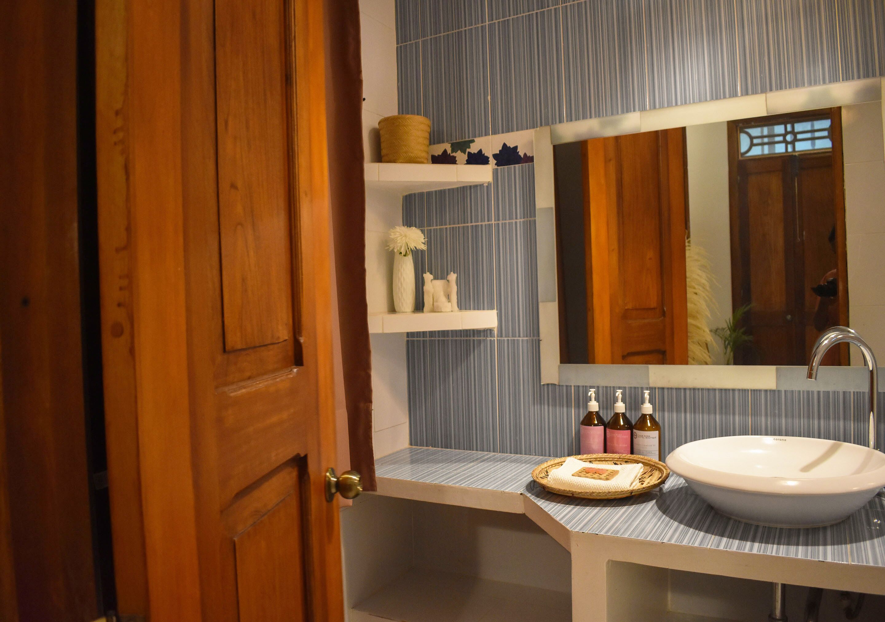 A bathroom with a wooden door, a blue-striped tile wall, a white sink, and a mirror above it.