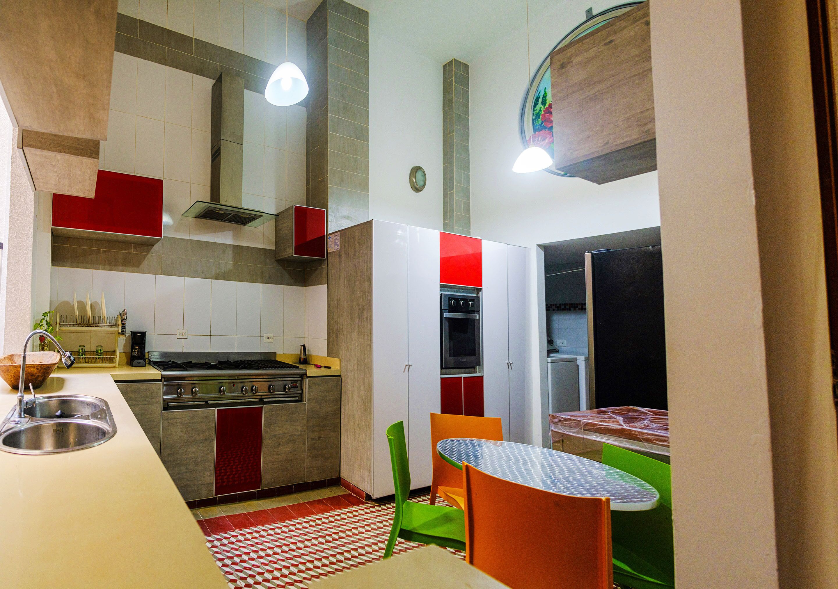 A compact kitchen with a stove, sink, and refrigerator, a dining area with a table and chairs, and a red and white checkered floor.