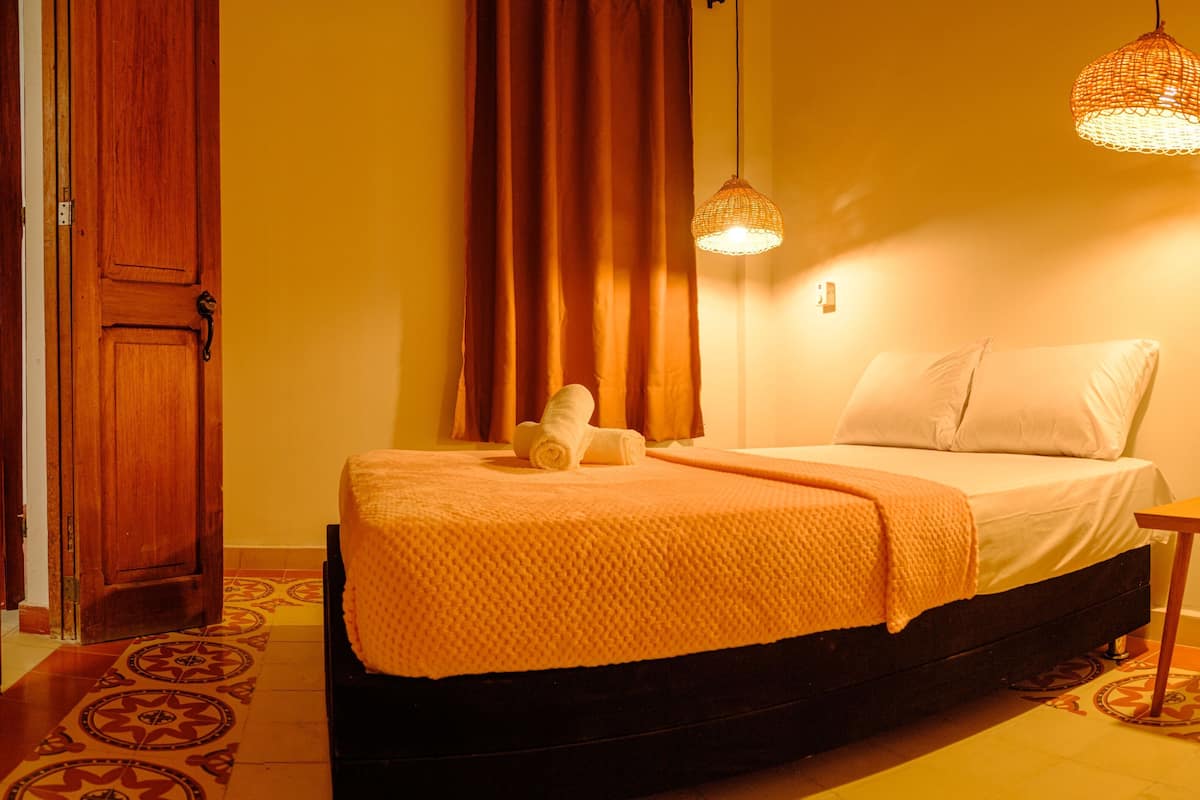 A room with a bed, a wooden door, a curtain, and a hanging light fixture.