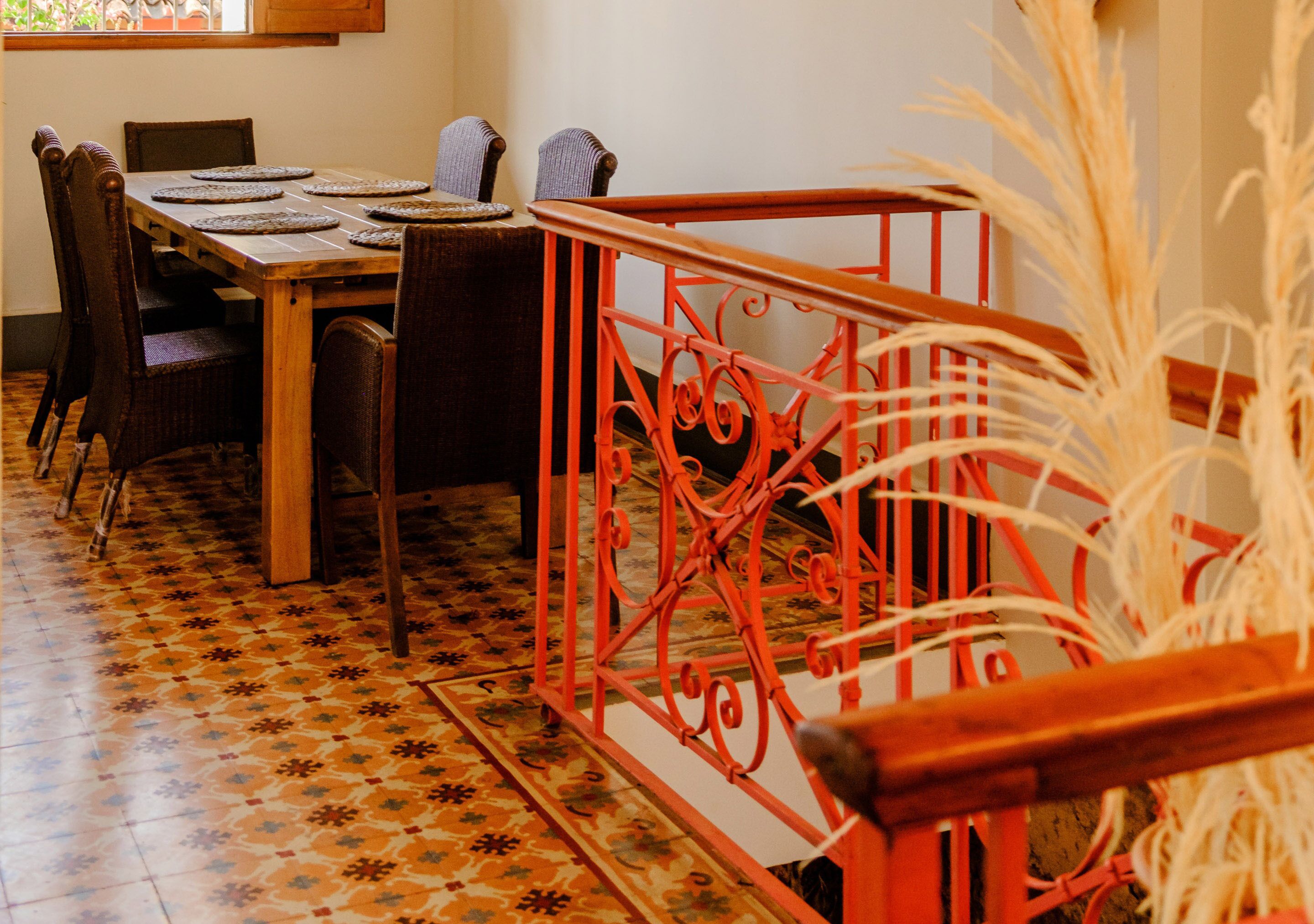Un comedor con una mesa de madera, sillas y una barandilla de metal rojo.