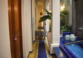 A narrow hallway with a tiled floor, a wooden door, a small table with chairs, and a blue tiled pool area with decorative balls.