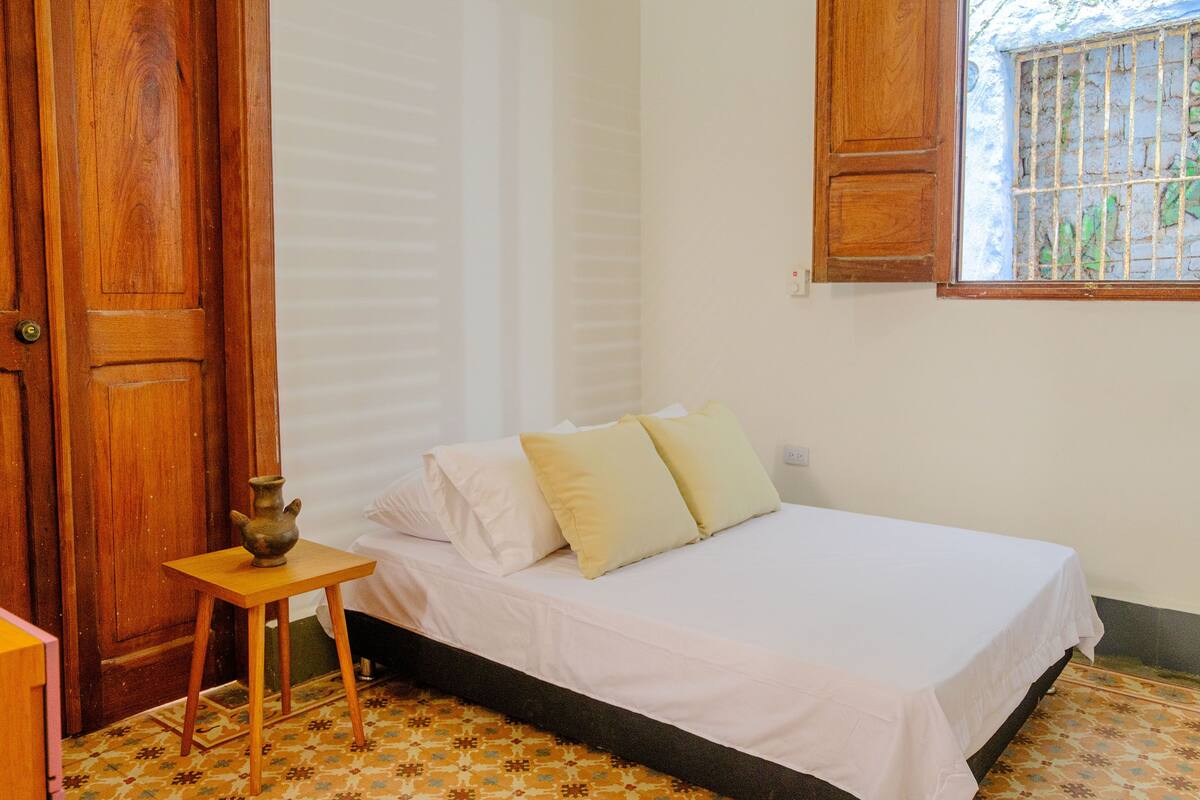 A bedroom with a bed, a small table, and a window with bars.