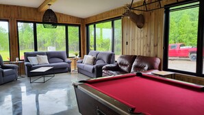 Une pièce chaleureuse avec une table de billard, deux canapés et une grande fenêtre ornée d’une tête de cerf fixée au mur.