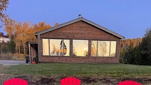 Une maison avec un foyer extérieur et trois chaises Adirondack rouges dans le jardin.
