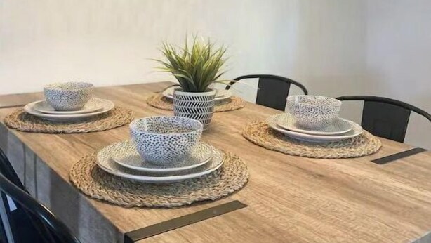 Un'area pranzo con un tavolo in legno, sottopiatti intrecciati e un lampadario intrecciato.