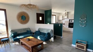 Ein modernes Wohnzimmer mit einer Sofagarnitur, einem Holztisch und einer Küchenzeile im Hintergrund.