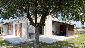 Ein Haus mit einer Terrasse, einem Baum und einer kleinen Sitzgelegenheit mit Stühlen und Tisch.