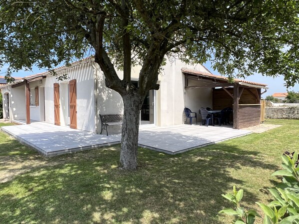 Una casa con patio, un árbol y una pequeña zona de estar al aire libre con sillas y una mesa.