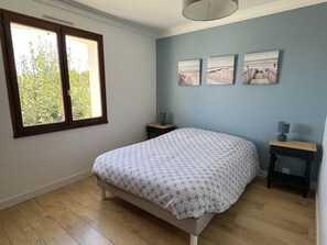 Un dormitorio con una cama, dos mesitas de noche, un ventanal y tres cuadros colgados en la pared.