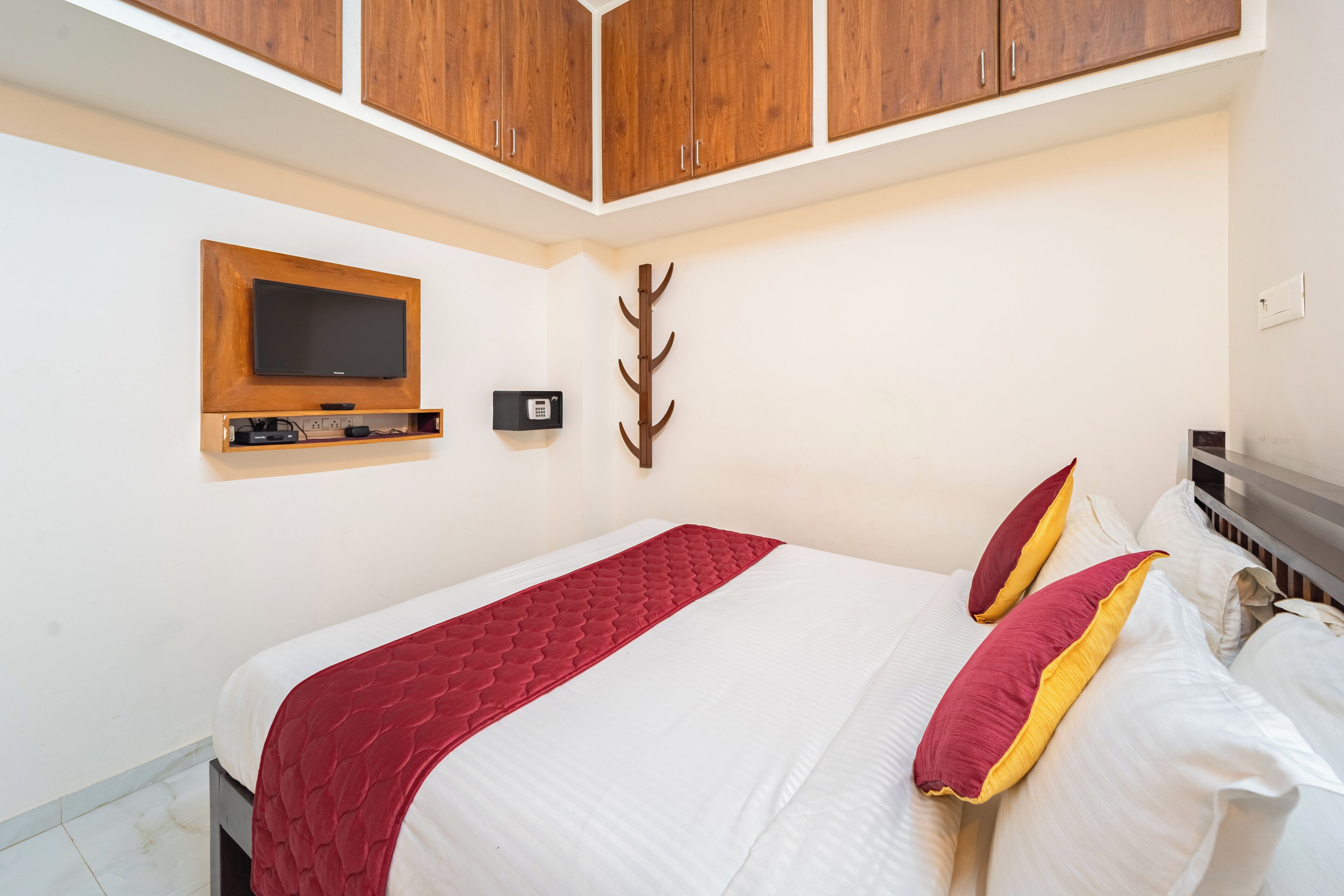 A neatly arranged bedroom with a bed, a mounted TV, and wooden cabinets above.