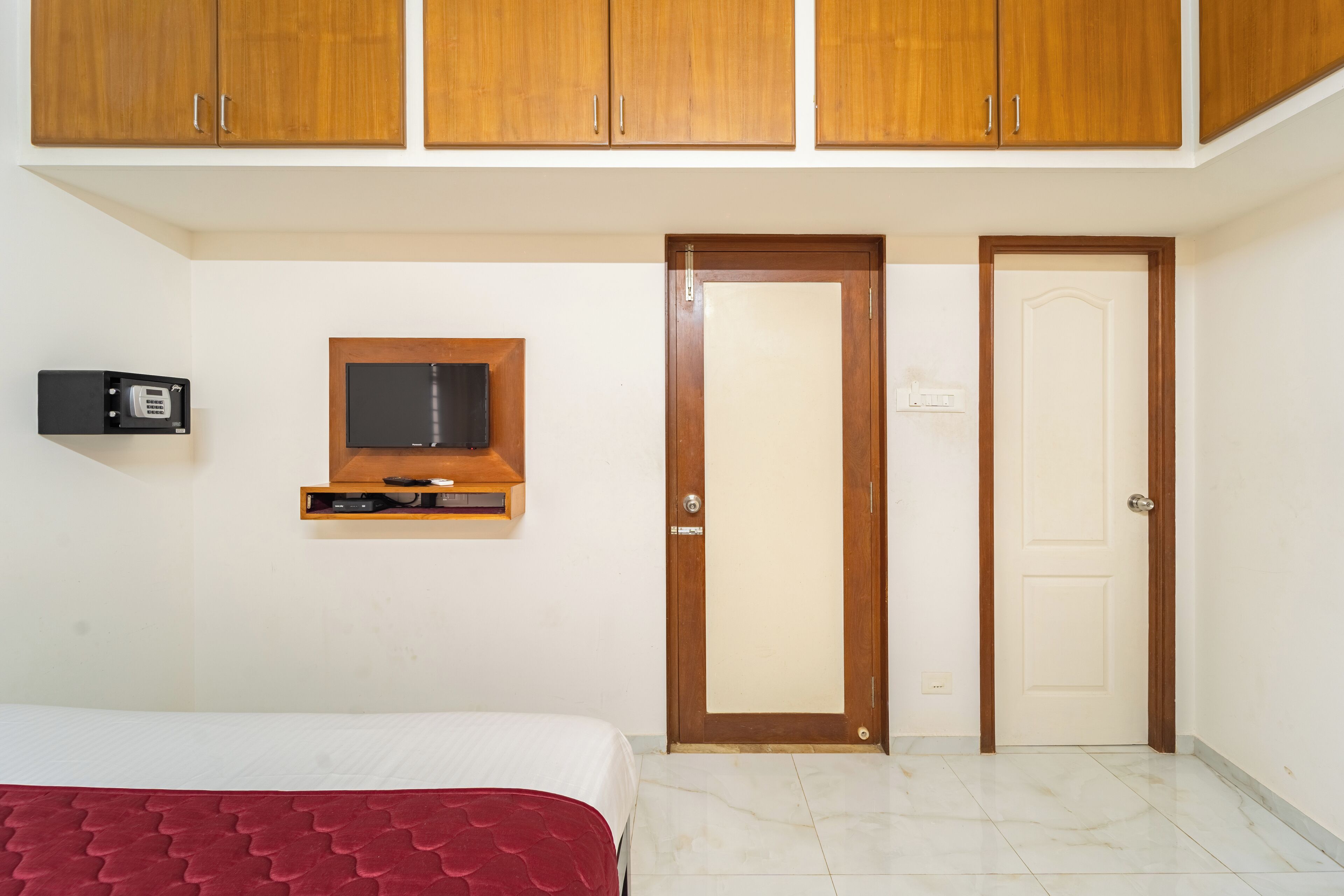 A bedroom with a bed, a wooden wardrobe, a television mounted on the wall, and a door.