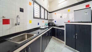 A kitchen with black cabinets, a stainless steel sink, a microwave, and a refrigerator. - Roscotel Shara Inn Pondicherry (Puducherry)