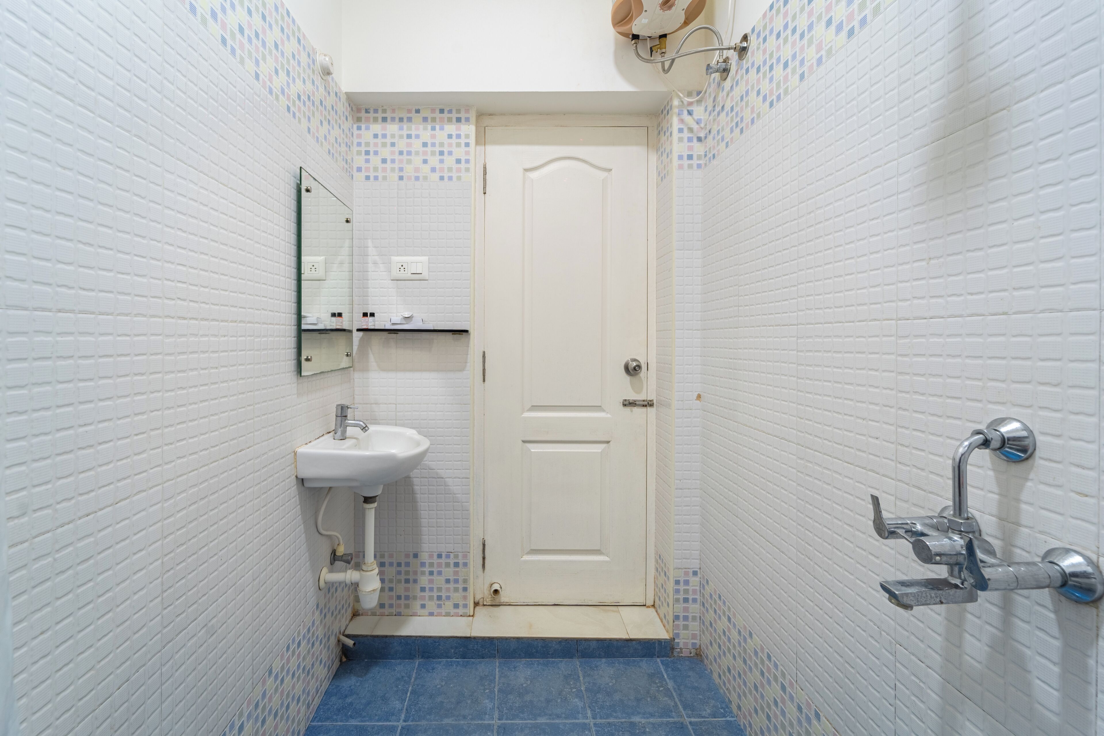 A small bathroom with white tiled walls, a white door, a sink, and a shower.