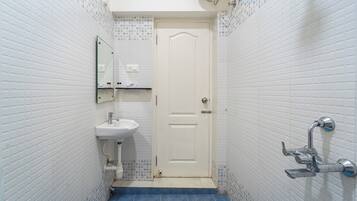 A small bathroom with white tiled walls, a white door, a sink, and a shower.