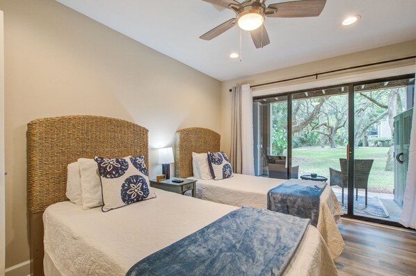 A hotel room with two beds, a ceiling fan, and a sliding glass door to the outside. - Seabrook Exclusives | 168 High Hammock (Seabrook Island)