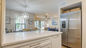 Una cocina moderna con un refrigerador de acero inoxidable grande, armarios blancos y una zona de comedor con un sofá azul.
