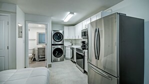 A compact kitchen with stainless steel appliances, a washer and dryer, and white cabinetry. - The Admiral Apartments (Jackson)