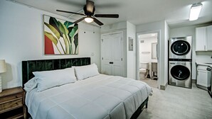 A bedroom with a bed, a ceiling fan, a wall-mounted artwork, and a laundry area with a washing machine. - The Admiral Apartments (Jackson)