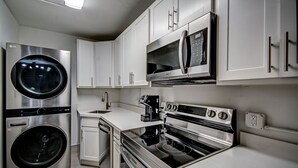 A modern kitchen with stainless steel appliances, including a washer, dryer, microwave, and oven. - The Admiral Apartments (Jackson)