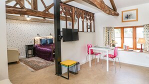 A room with a bed, a TV, a dining table with chairs, and a window with curtains. - The Forge (Taunton)