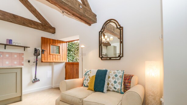 A living room with a beige sofa, wooden beams on the ceiling, a mirror, and a window with a view of greenery. - The Forge (Taunton)