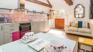 A kitchen with wooden beams, a dining table with floral tableware, and a sofa in the adjacent living area. - The Forge (Taunton)