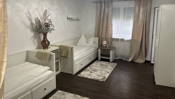 Een knus slaapkamer met een bed, nachtkastje, lamp en een klein raam met gordijnen.