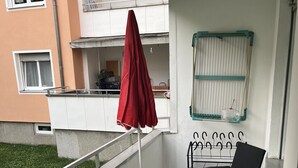 Een balkon met een tafel en stoelen, een rode parasol en een kleine tuin zichtbaar achter het hekwerk.