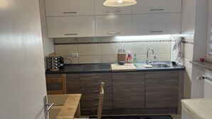 Een kleine keuken met witte kastjes, een zwart aanrecht, een ingebouwde kookplaat en een hanglamp.