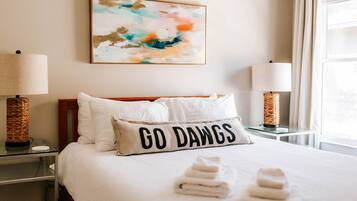 Hotelkamer met een bed, twee bedlampen, een wanddecoratie in abstractie stijl, en een kussen met de tekst 'GO DAWGS'.