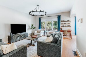 Een moderne woonkamer met een grote flatscreen-tv, een kroonluchter en een zithoek.
