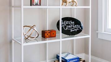 Een witte boekenkast met verschillende spullen, waaronder boeken, een bord met een welkomstboodschap, een voetbalhelm, een beeldje van een hond, dobbelstenen en een bord van een brouwerij.