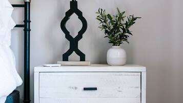 A white bedside table with a drawer, a black lamp with a white shade, and a potted plant.