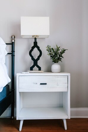 A white bedside table with a drawer, a black lamp with a white shade, and a potted plant. - Master on Main + 2 Living Rooms I Minutes to Downtown, UGA & Sanford I Sleeps 9 (Athens)