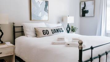 Een net opgemaakt bed met een kussen waarop 'GO DANGS' staat, een bedlampje en abstracte kunst aan de muren.