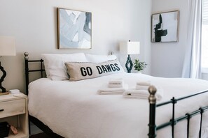 Un lit bien fait, avec un oreiller sur lequel on peut lire « GO DANGS », une lampe de chevet et des œuvres d’art abstraites accrochées aux murs.