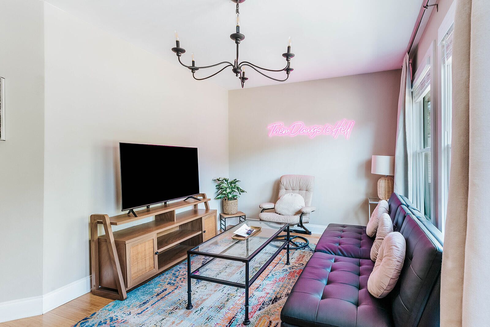 Ein modernes Wohnzimmer mit einem Flachbildfernseher, einem Sofa, einem Sessel, einem Couchtisch und einer Deckenleuchte.