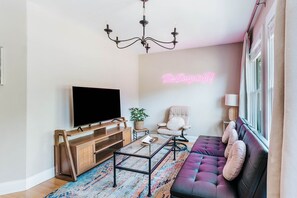 Een moderne woonkamer met een flatscreen televisie, een bank, een fauteuil, een salontafel en een kroonluchter.