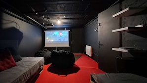 A dimly lit room with a projector screen, a red carpet, and a couch with pillows. - 15-P Chalet, 7BRs, Jacuzzi, Sauna, Prime Loc, Quiet, Cleaning & Linens Incl. (Les Deux Alpes)