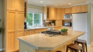 Una cocina con armarios de madera, una isla central, un microondas, un refrigerador y una ventana con vista a la vegetación.
