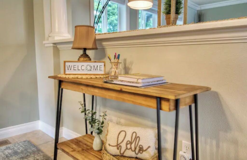 A wooden console table with a 'WELCOME' sign, a lamp, and a notebook.