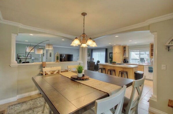 Enjoy meals in this dining area with a long table and comfortable seating for four, surrounded by a modern kitchen and living space.