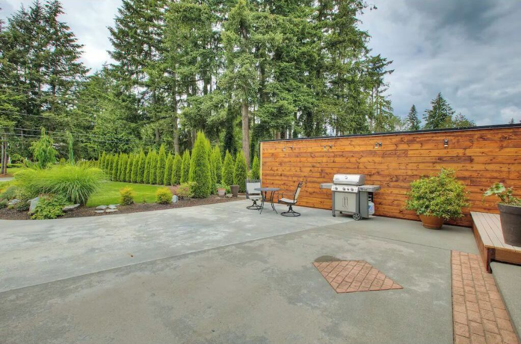 Un patio con pared de madera, una parrilla y mobiliario de exterior.
