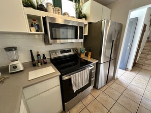 Eine moderne Küche mit Edelstahlgeräten, darunter eine Mikrowelle, ein Backofen und ein Kühlschrank. Über der Arbeitsfläche befinden sich Schränke, und ein Mixer ist auf der linken Seite sichtbar.