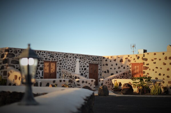 A stone building with a wooden door and a white umbrella. There is a lamp post in the foreground. - Hotel Rural El Cabo (La Oliva)